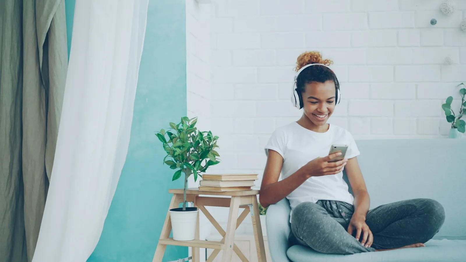 A listener relaxing on a sofa with headphones and a phone