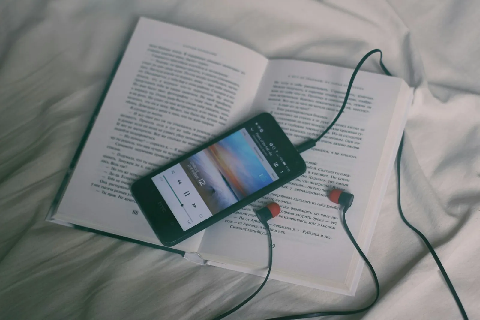 A phone playing an audiobook on top of an open book with earphones